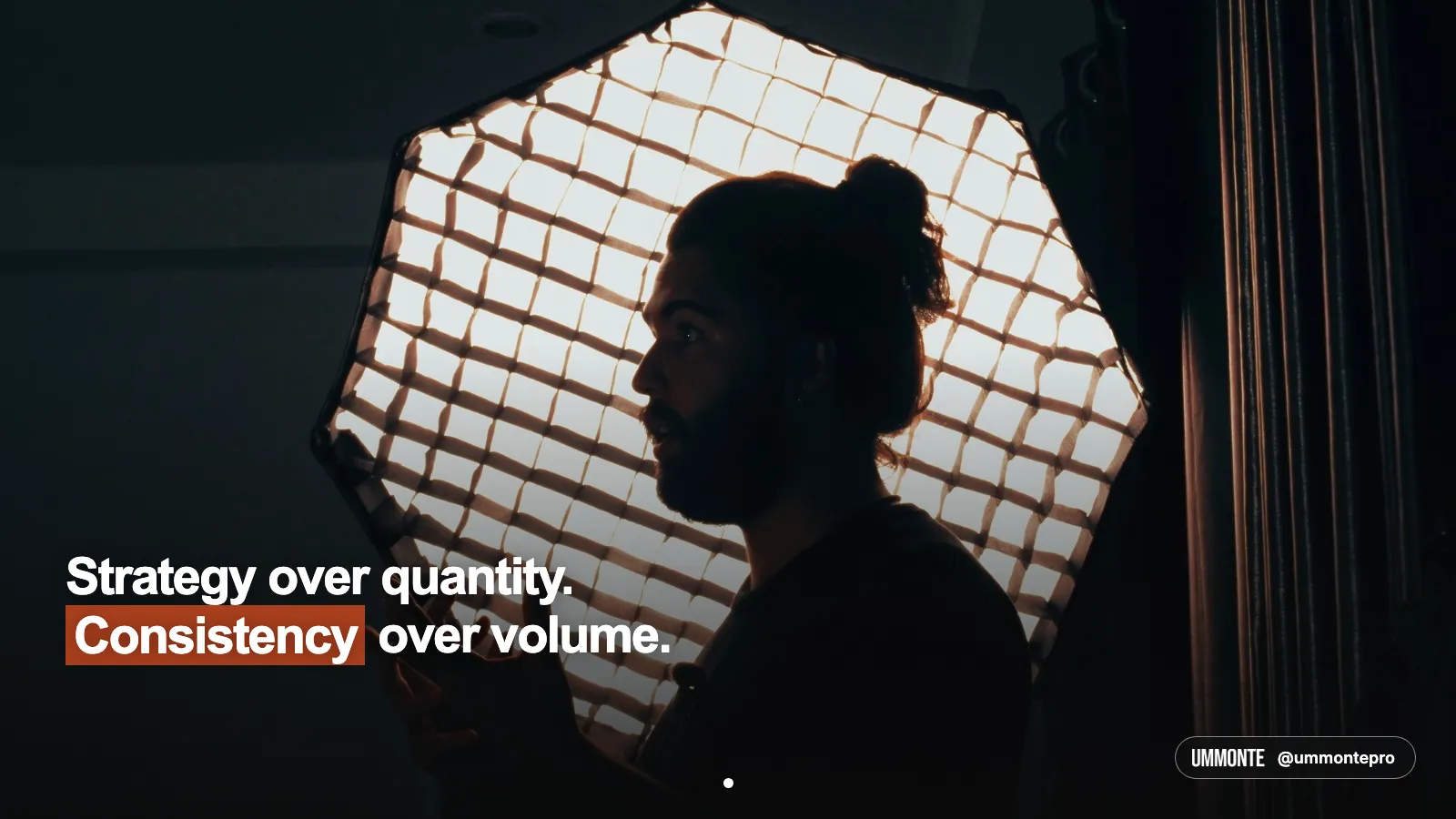 Strategy over quantity, consistency over volume, in bold white type with consistency highlighted in orange, silhouette of a man talking in front of a glowing softbox